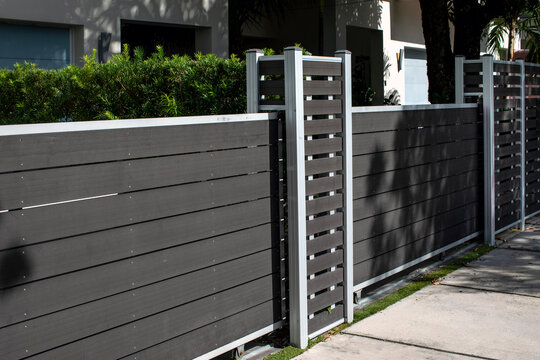 Modern dark composite privacy fence with horizontal slats and metallic posts along a sidewalk