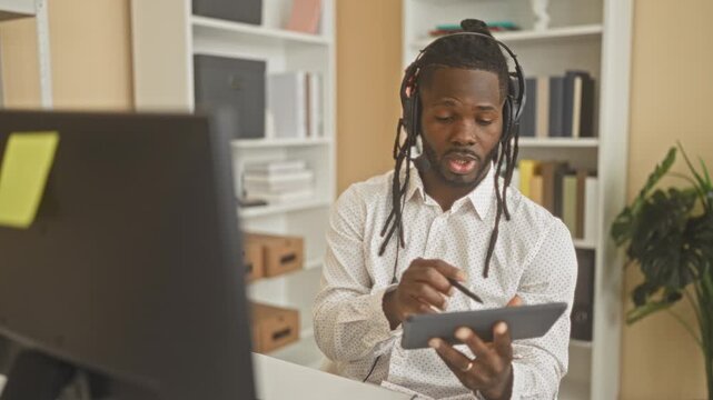 Young man with headset writing on tablet with stylus, hand visible in studio; focused collaboration.