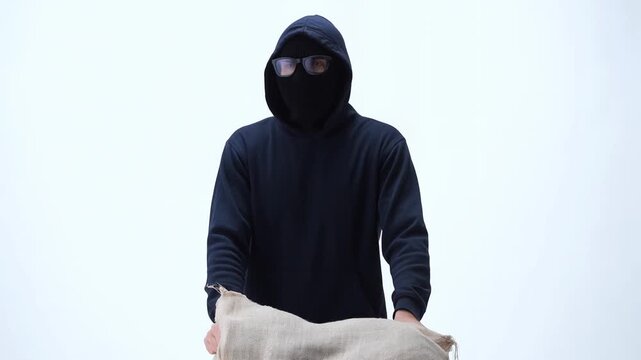 Masked person holds burlap sack while standing against plain white background
