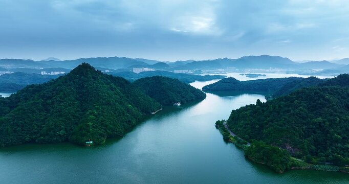 Aerial view of lush green forested hills surrounding a winding blue lake under a cloudy sky in soft natural light.