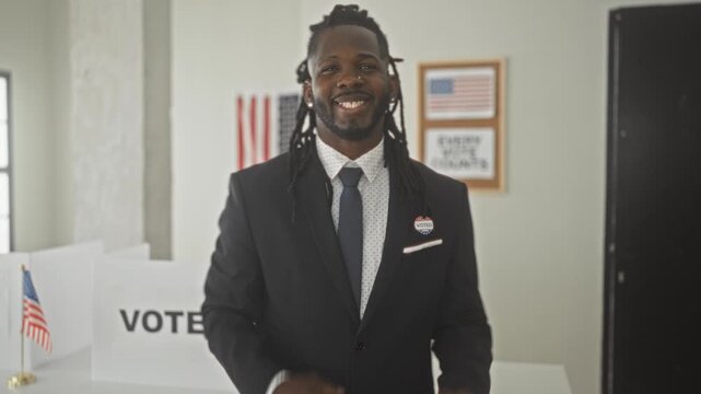 Man in suit wearing voted sticker gives a thumbs up while smiling beside vote sign in polling building; civic pride.