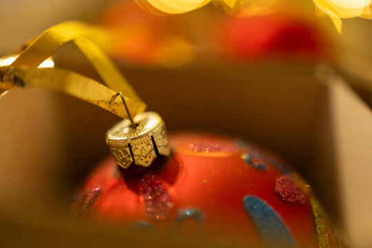 Close-up of red Christmas baubles in a box with warm bokeh lights in the background.