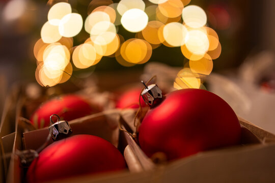 Close-up of red Christmas baubles in a box with warm bokeh lights in the background.