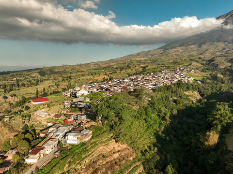 Aerial view of Kruwisan village nestled on the lush green slopes of the mountain with terraced fields and traditional houses in Kledung, Central Java, Indonesia.