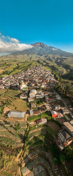 Aerial view of Kruwisan village nestled in the lush terraced hills of Central Java with a majestic mountain backdrop under a clear blue sky, Kledung, Central Java, Indonesia.