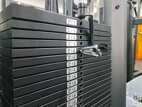 Stacked weight plates rest neatly on gym equipment. Black metal plates marked with weight values align vertically. Chain connects plates for secure stacking and safe handling