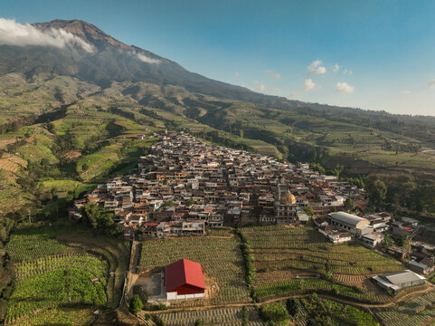 Aerial view of Kruwisan village nestled among terraced agricultural fields with a majestic mountain in the background in Kledung, Central Java, Indonesia.