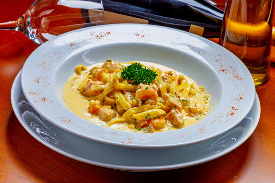 Exquisite creamy shrimp pasta garnished with fresh herbs, elegantly plated in a white bowl on a wooden table, with wine in the background.