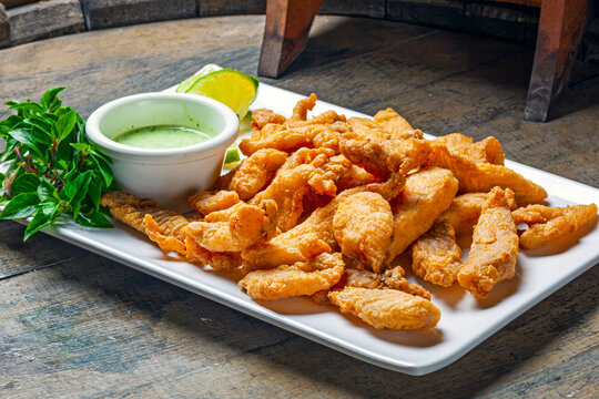 Description
Crispy fried fish strips served with green dipping sauce and lime on a rustic wooden table. Traditional bar food appetizer.