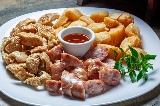 Traditional Brazilian bar appetizer platter with sliced sausage, crispy pork rinds, fried cassava, and a small bowl of hot pepper sauce on a white plate over a rustic wooden table.

Keywords
