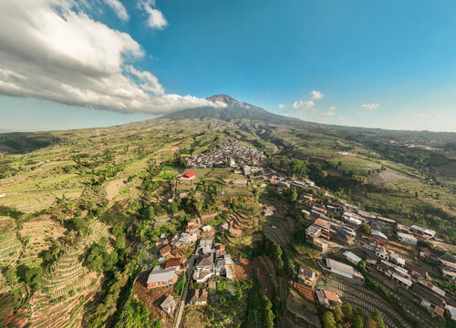 Aerial view of Kruwisan village nestled on the slopes of Mount Sindoro with terraced agricultural fields and lush green landscape in Kledung, Central Java, Indonesia.