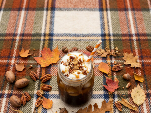 Enjoy an iced pecan crunch latte with whipped cream on plaid blanket, a delicious Fall drink, new flavor perfect for cozy autumn afternoon