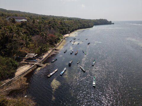 Aerial view of traditional wooden fishing boats moored along the lush tropical coastline of Tomia Timur, South East Sulawesi, Indonesia.