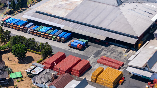 Aerial view of a logistics warehouse facility with a line of parked trucks and stacks of red and yellow materials in Salatiga, Central Java, Indonesia.