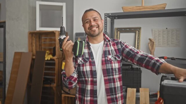 Man carpenter holds cordless drill and extends arm toward toolbox in building workshop; pride craftsmanship.