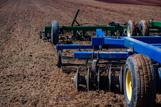 Countryside agriculture. Heavy farm machinery. Blue agricultural machine. Farm wheel detail. Metal frame equipment. Disc gang harrow. Soil cultivation equipment. Ground preparation machinery.