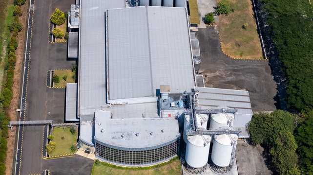 Aerial view of an industrial factory complex featuring large metal storage silos, a flat-roofed warehouse building, and paved access roads in Salatiga, Central Java, Indonesia.