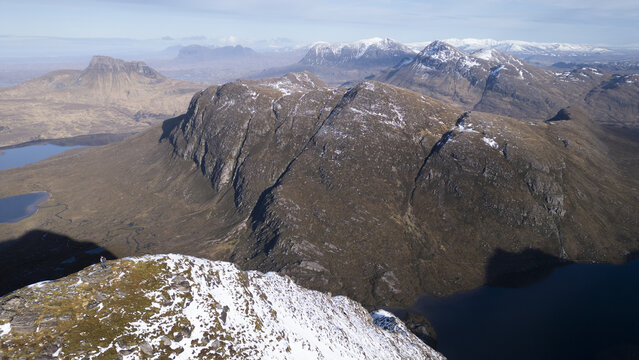 Aerial view of Ben Mor Coigach with snow-dusted peaks, rugged mountain ridges, and dark lochs in Ullapool, Scotland, United Kingdom.