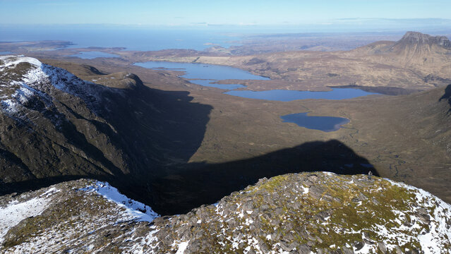 Aerial view of the rugged mountainous landscape of Ben Mor Coigach with snow-dusted peaks and deep blue lochs in the Scottish Highlands, Ullapool, Scotland, United Kingdom.