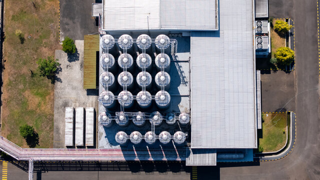 Aerial view of industrial storage tanks arranged in a grid pattern next to a large warehouse facility with metal roofing and paved grounds in Salatiga, Central Java, Indonesia.