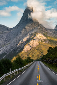 Aerial view of Stetind mountain surrounded by clouds and autumn foliage with a road leading towards the peak in Narvik Municipality, Nordland, Norway.
