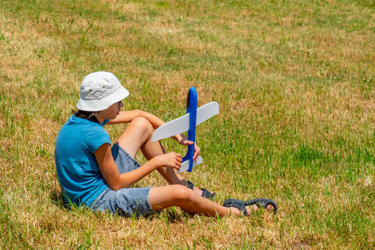 sad teenage boy sitting on dry grass in sunny park, foam glider plane, disappointment fun activity goes wrong, isolation outdoors, feeling exhausted, youth burnout, summer fatigue, adolescent stress