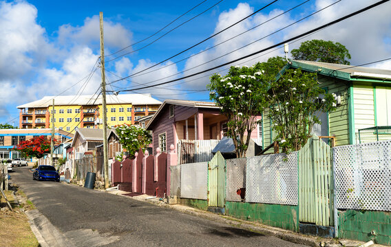 Traditional colorful wooden houses and fences along a residential hillside street in Saint John Antigua and Barbuda under a blue sky.