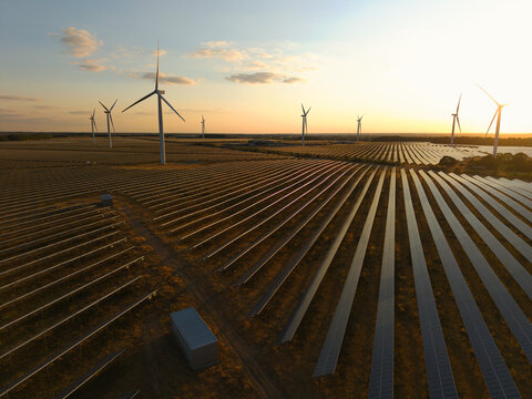 Aerial view of wind and solar renewable energy park at sunset with rows of photovoltaic panels and wind turbines in Chelveston, England, United Kingdom.