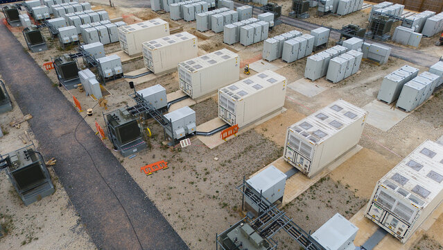 Aerial view of a battery energy storage facility and electrical substation with rows of white storage containers and power infrastructure in Stony Stratford, England, United Kingdom.