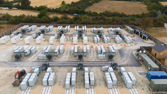 Aerial view of a battery energy storage facility and substation with rows of white containers and electrical transformers on a gravel site in Stony Stratford, England, United Kingdom.