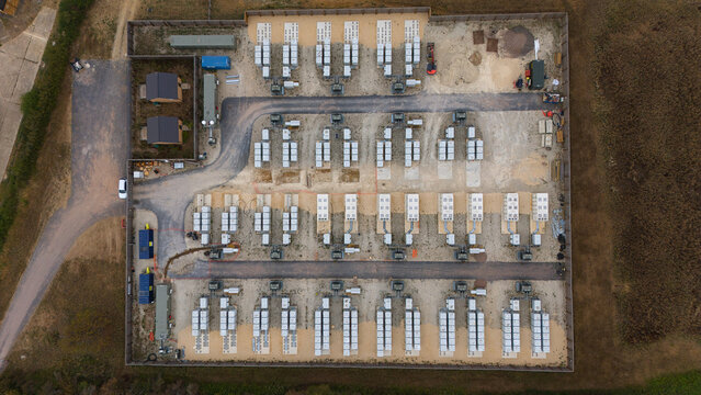 Aerial view of a battery energy storage facility with rows of white storage units and electrical infrastructure on a gravel site in Stony Stratford, England, United Kingdom.
