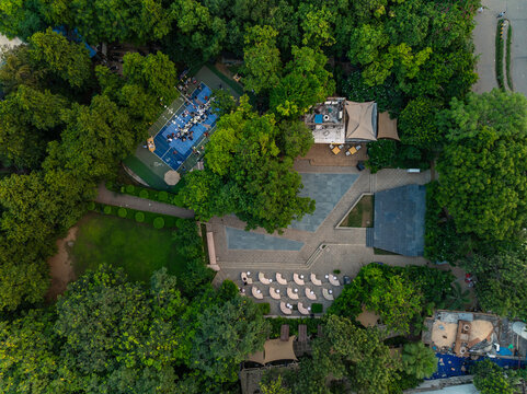 Aerial view of an outdoor event space with a blue court and curved seating arrangements nestled among lush green trees in New Delhi, Delhi, India.
