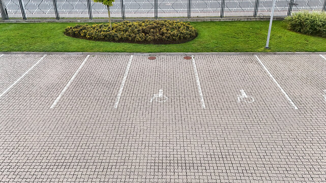 Aerial view of a paved parking lot with marked handicap parking spaces, adjacent to a green lawn and a metal fence in Riga, Latvia.