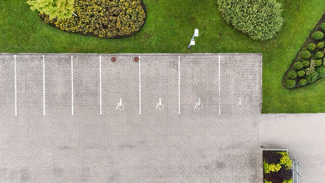 Aerial view of a parking lot with clearly marked handicap parking spaces, paved with grey interlocking bricks, surrounded by manicured green grass in Riga, Latvia.