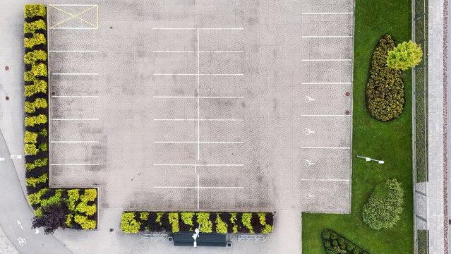 Aerial view of an empty parking lot with marked spaces, including accessible parking spots, bordered by manicured hedges and green lawns in Riga, Latvia.