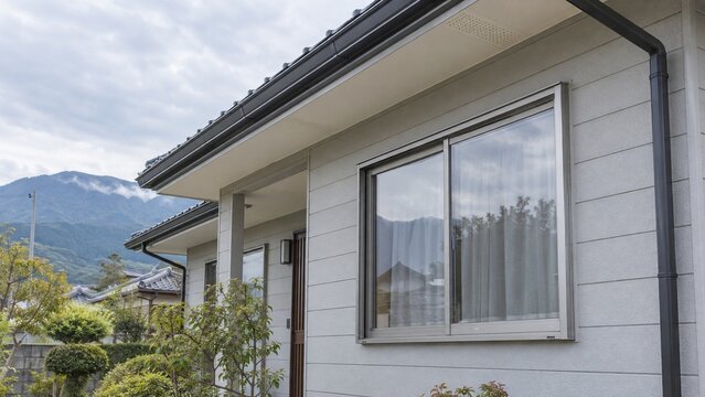 山並みを背景に白い外壁と窓が並ぶ住宅の軒先と雨樋