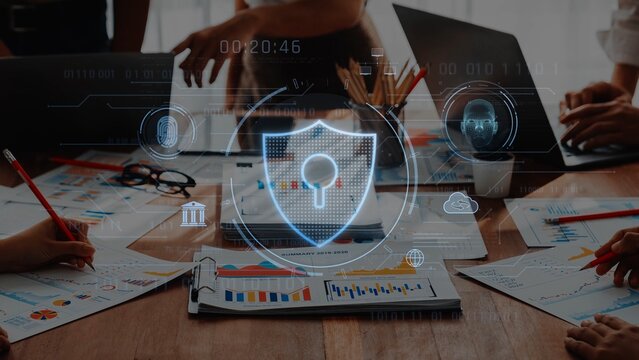 A business team works together analyzing data with cybersecurity visuals on a laptop, showcasing innovative collaboration in a modern workspace focused on protection and strategy. Raster