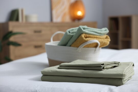 Home textile. Fresh clean towels in basket and linens on bed, selective focus