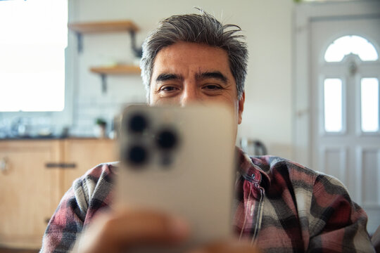 Smiling middle-aged man using smartphone in home kitchen
