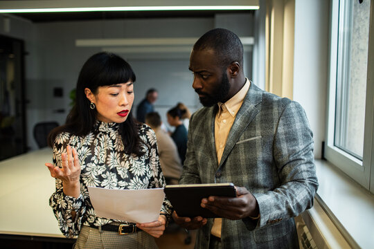 Two coworkers reviewing report on tablet by modern office window