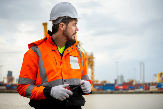 Engineer man in hard hat holding walkie talkie at container port terminal, Dock worker in reflective vest and safety helmet working at shipping port, Logistic manager at industrial cargo yard