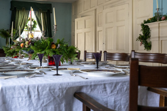 A large dinner table set for a festive Christmas celebration. The linen is white cotton, the centerpieces are made from natural greenery, fruit, and berries. A large candelabra sits in the middle.