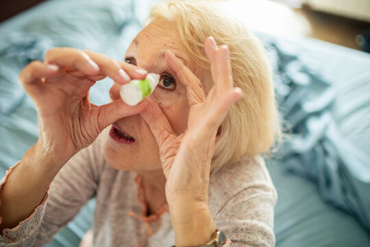 Senior woman applying eye drops at home in bedroom