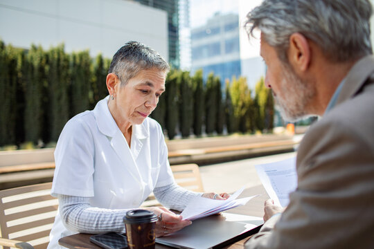 Two senior professionals reviewing documents at outdoor city cafe