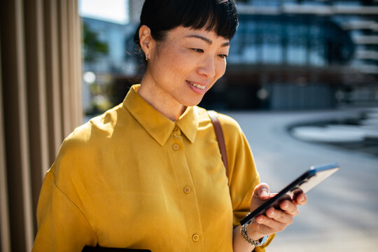Smiling businesswoman using smartphone outside modern office
