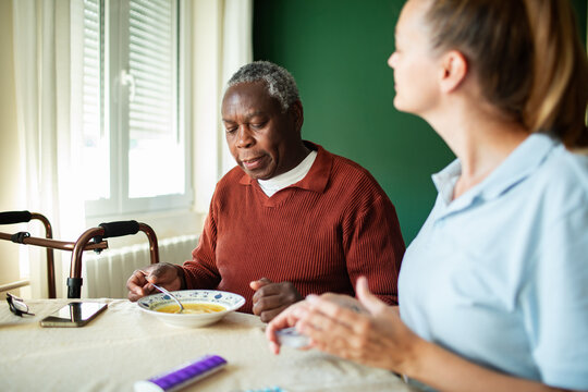 Caregiver helping senior man eat soup at home