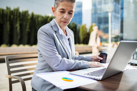 Senior businesswoman working on laptop outdoors in urban office plaza