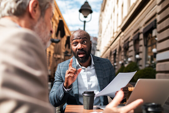 Two businessmen arguing over documents at outdoor cafe