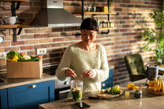 Woman making healthy green smoothie at home kitchen