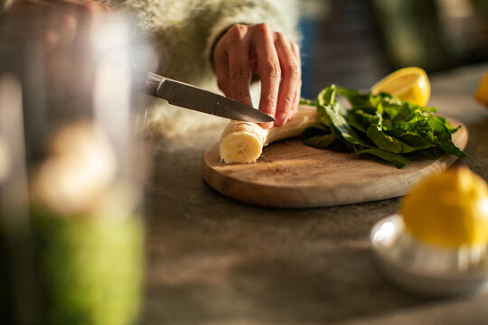 Person slicing banana for green smoothie in kitchen